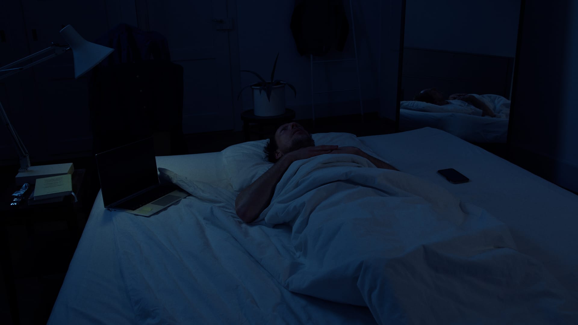 Ein wacher Mann liegt nachts in einem dunklen Schlafzimmer im Bett.