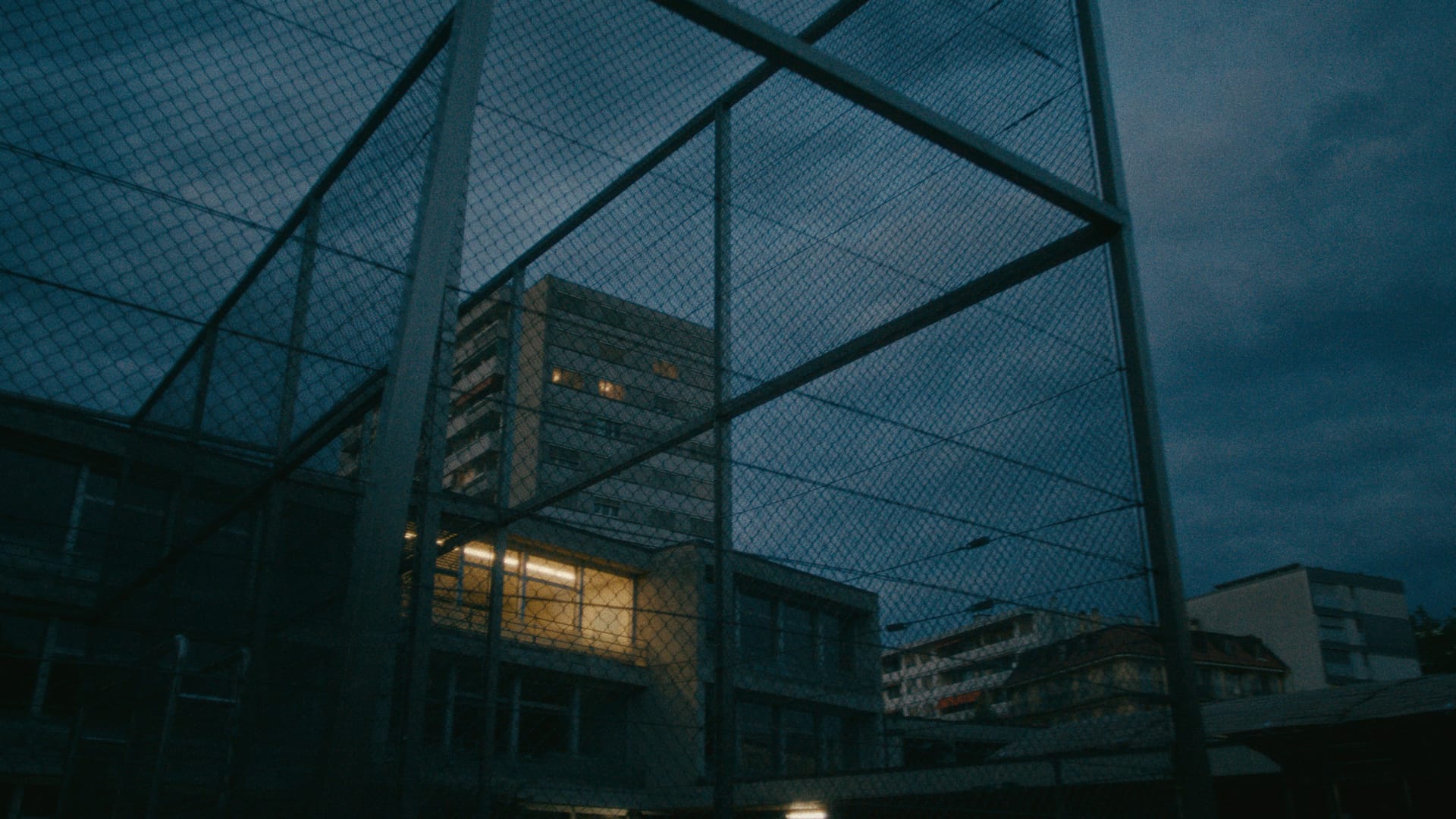 Ein institutionelles Gebäude hinter einem hohen Metallzaun in der Dämmerung.