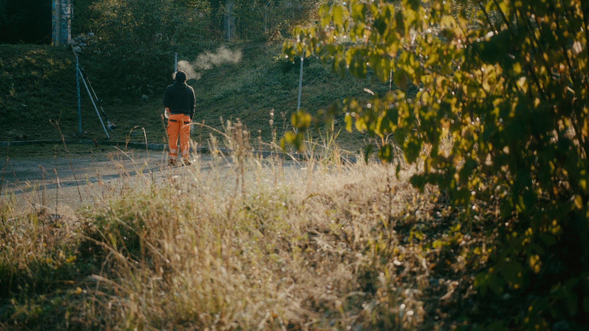 Eine Person in orangefarbener Arbeitskleidung überquert eine trockene Wiese.