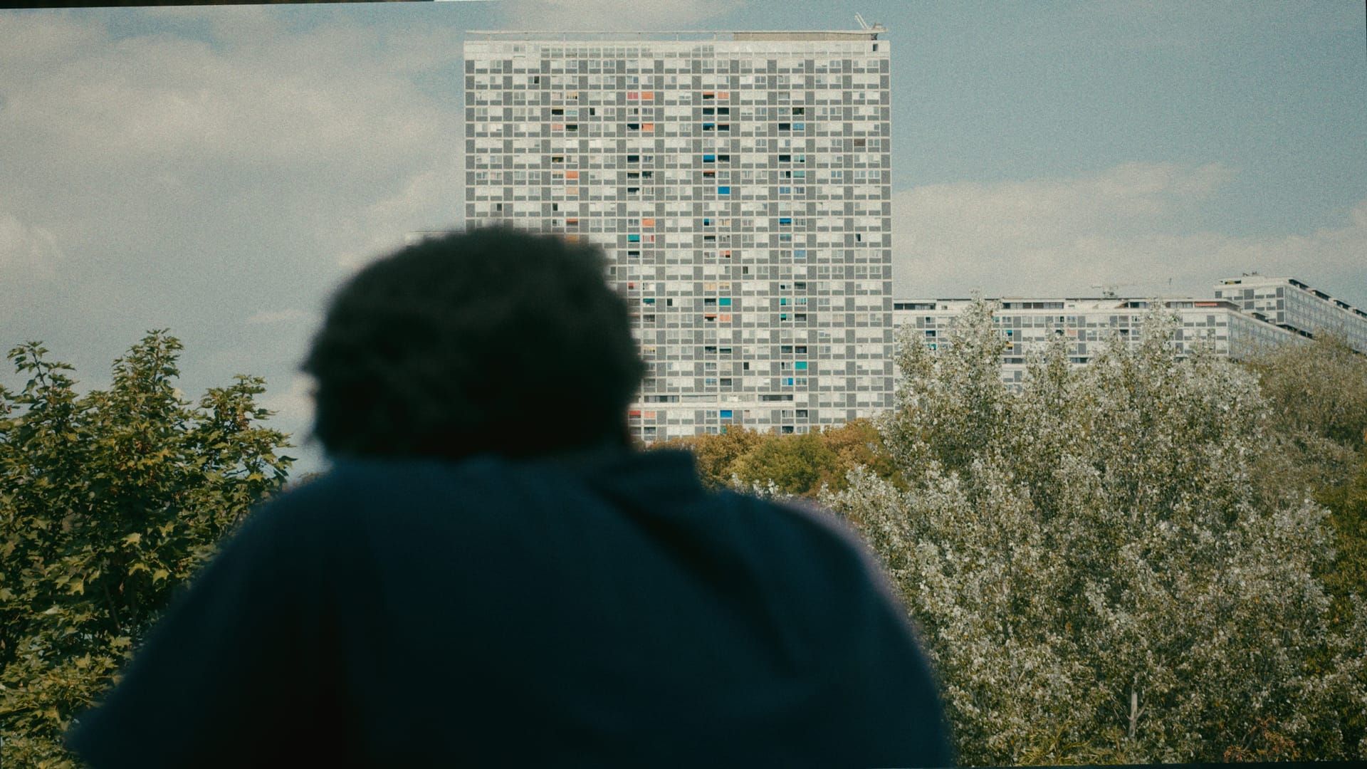 Eine Person blickt von einer Terrasse auf ein grosses Wohnhochhaus.