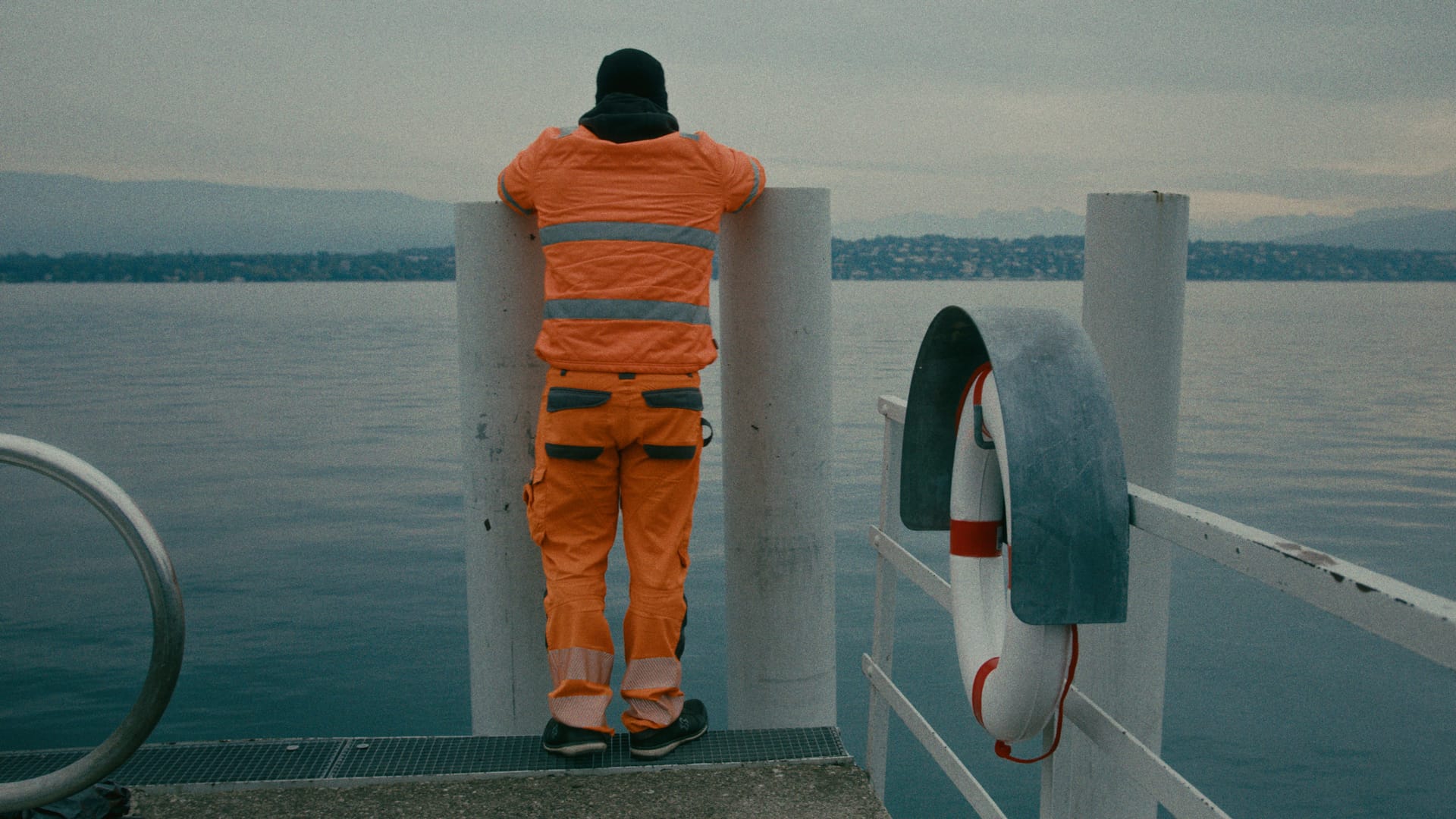 Eine Person in orangefarbener Arbeitskleidung blickt vom Deck eines Schiffs über den See.